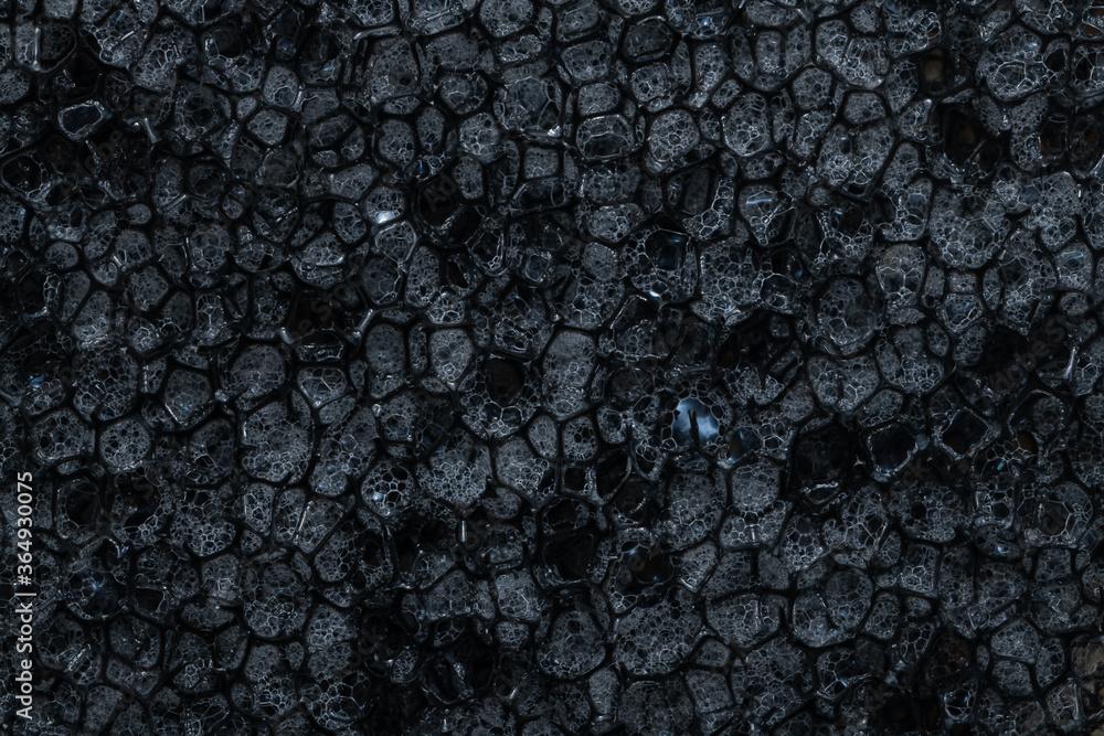 Household dishwashing sponge from reticulated foam, texture, background. Surface of black sponge for washing dishes, pattern closeup