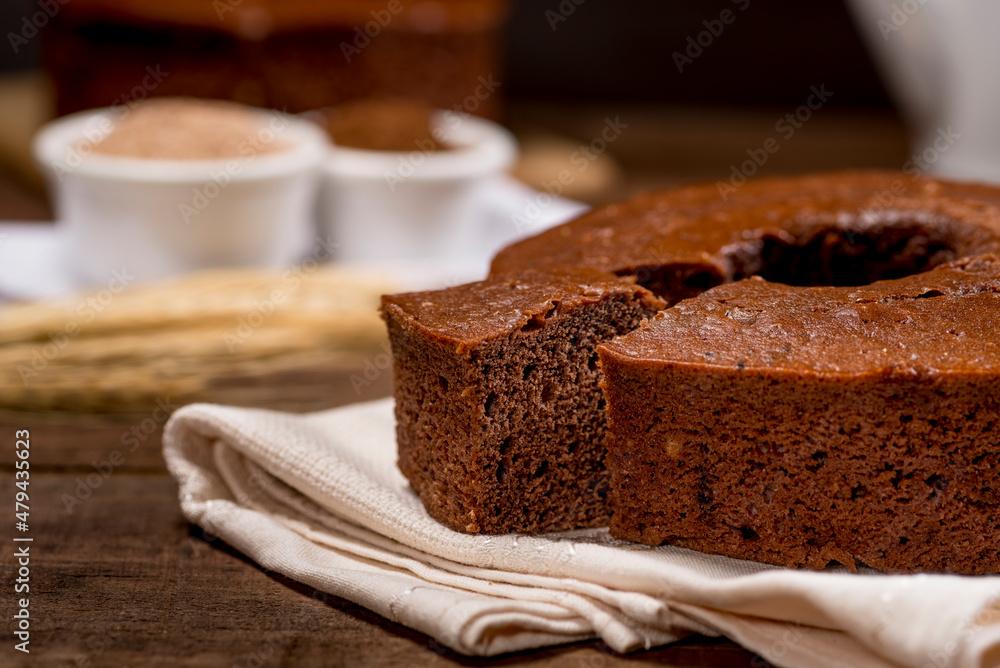 chocolate cake and slice on fabric on wood with cake in the background with wheat branch beside