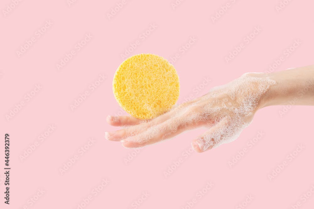 Hand of an anonymous woman with foam and a yellow sponge