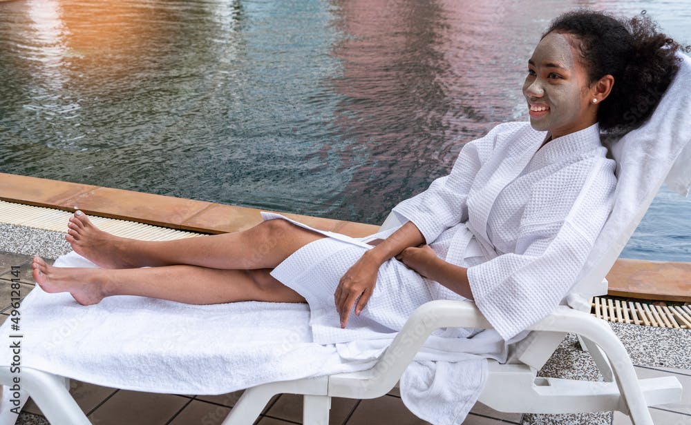 African american girl relaxing face mask, wearing a white bathing suit, lounging by the pool. 