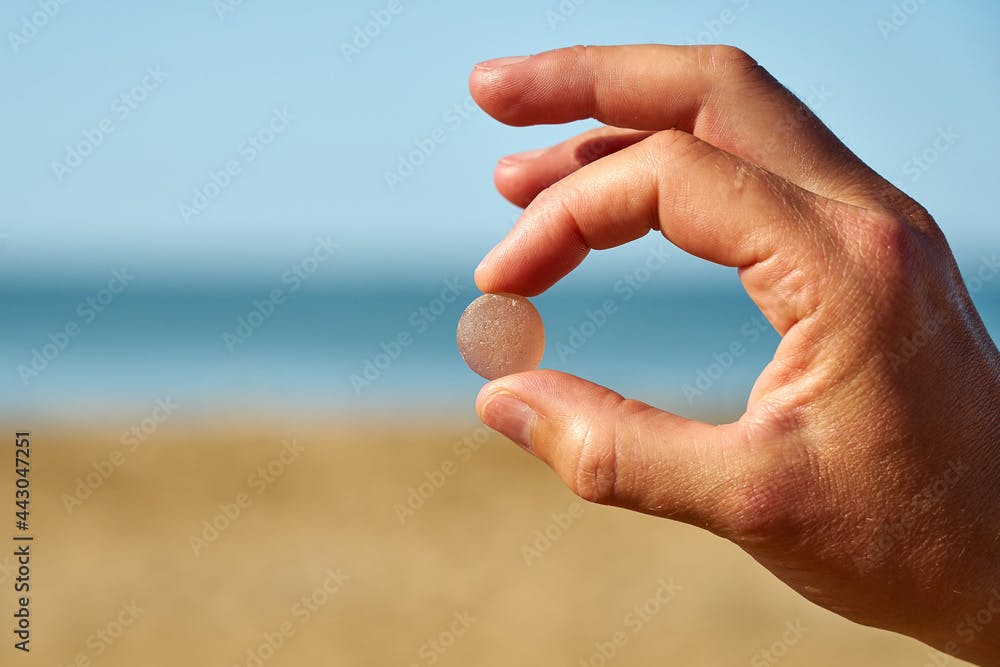 A person holds a single piece of pink sea glass between their finger and thumb