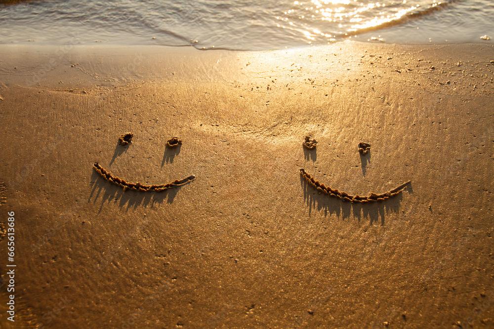 two emoticon happy smile face painted on jetted beach sand by sea