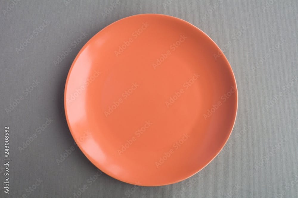 Empty coral color plate on the grey background.Top view.Copy space.Diet minimal concept.