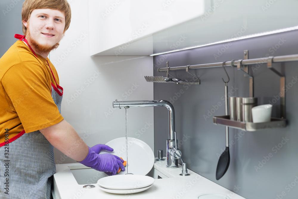 young man with red beard  washes dishes on white modern kitchen