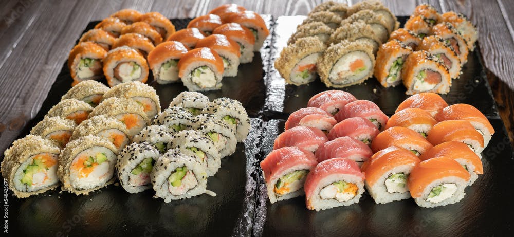 Rainbow Sushi Roll set with salmon, eel, tuna, avocado, royal prawn, cream cheese Philadelphia on black stone board.