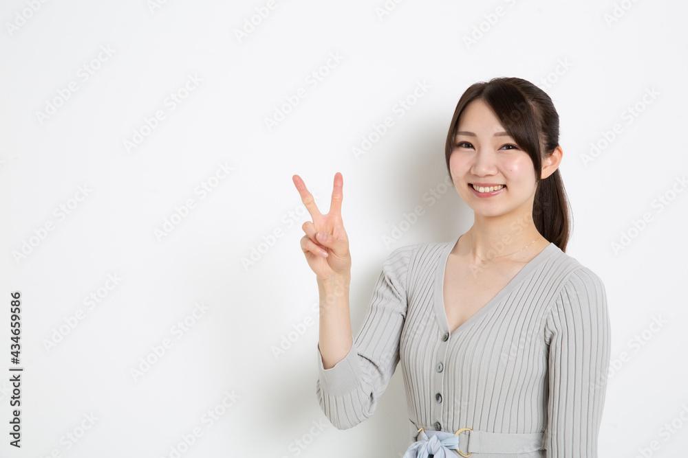 笑顔で指を2本立てているポニーテールの女性