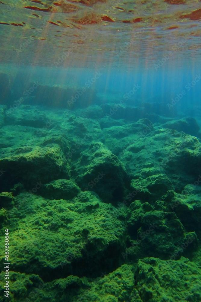 Underwater scenery with stones formation and sunrays from the surface. Picture from snorkeling, sun and rocks in the ocean. Water and sunlight. Seascape in the morning.