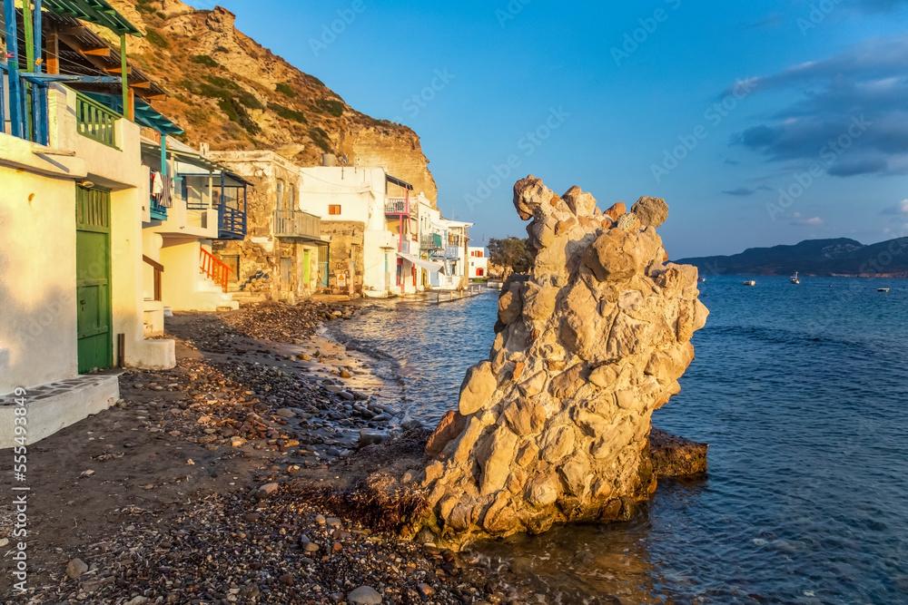 Rock formation and houses along the water's edge on the coast of Milos; Milos, Greece