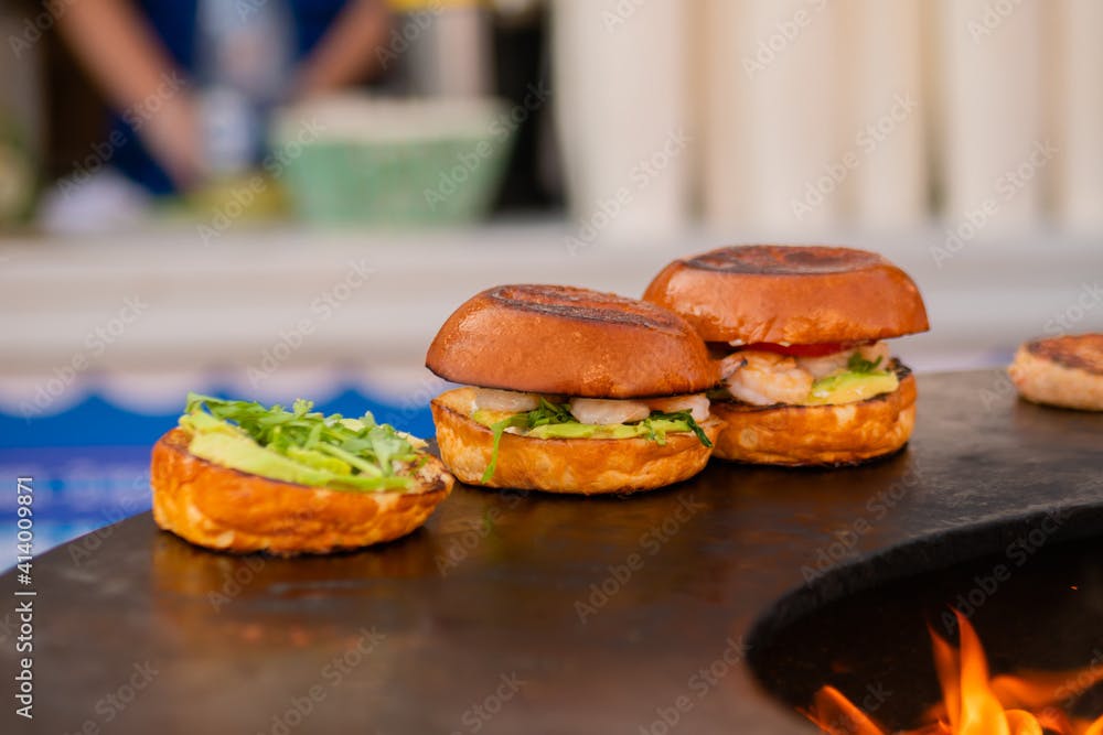 Process of preparing fish burgers with shrimp, prawn on brazier with hot flame at summer local food market - close up view. Outdoor cooking, seafood, gastronomy, cookery, street food concept