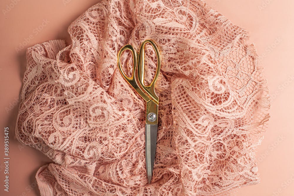 Flat lay of tailoring scissors placed on top of wrinkled coral color lace fabric with patterns